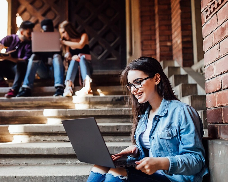 Smiling student using laptop on campus steps, guided by study abroad consultants in Kochi